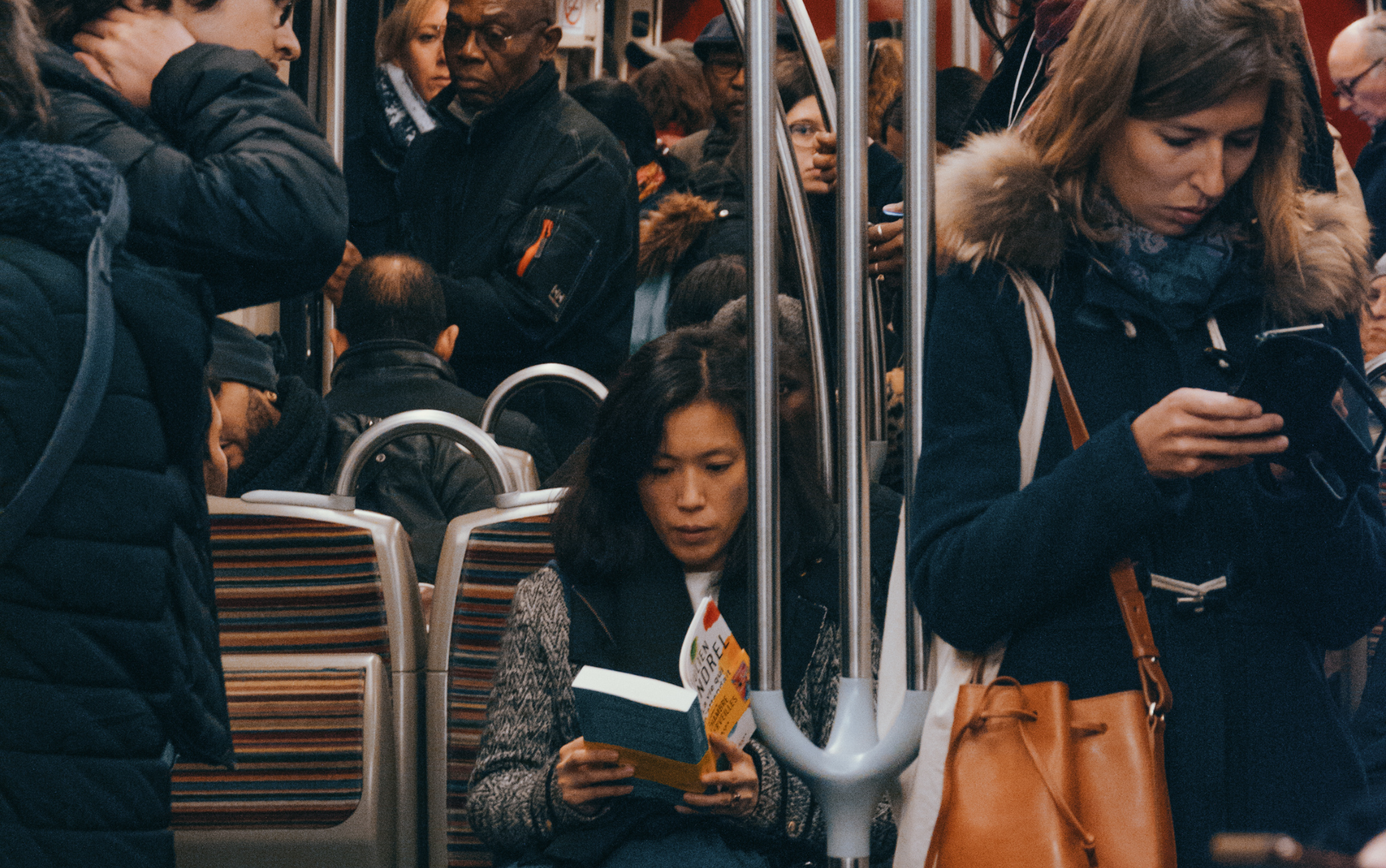 Plan d'un métro bondé, focus sur deux femmes : l'une à l'air passionné par son livre, l'autre à l'air blasé derrière son smartphone