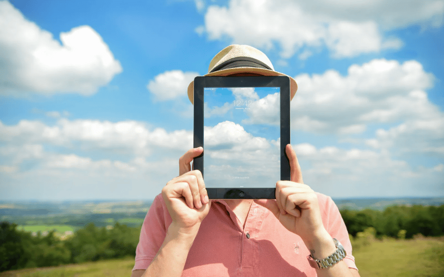 Portrait d'un homme tenant une tablette électronique devant son visage, du même motif que le ciel en arrière plan (homme invisible)
