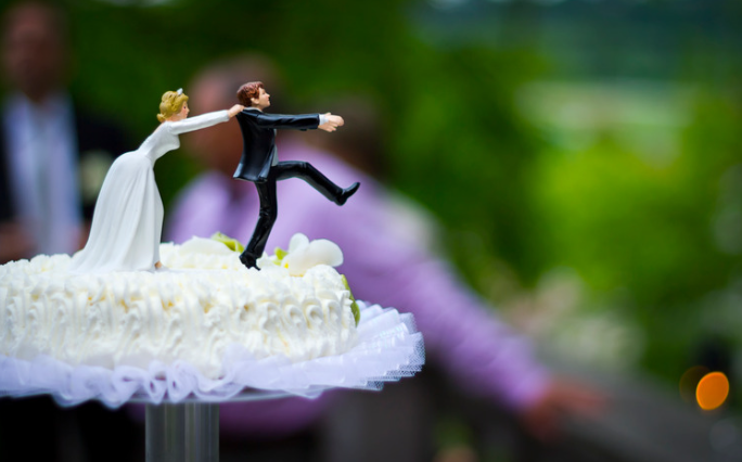 Deux figurines sur un gâteau de mariage : l'époux essaie de fuir, tiré par les épaules par son épouse